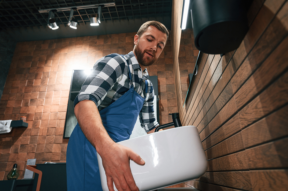 holding-and-moving-a-sink-plumber-in-blue-uniform content-image